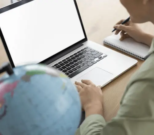 Student writing notes beside a laptop and a globe, preparing a diploma translation to study abroad
